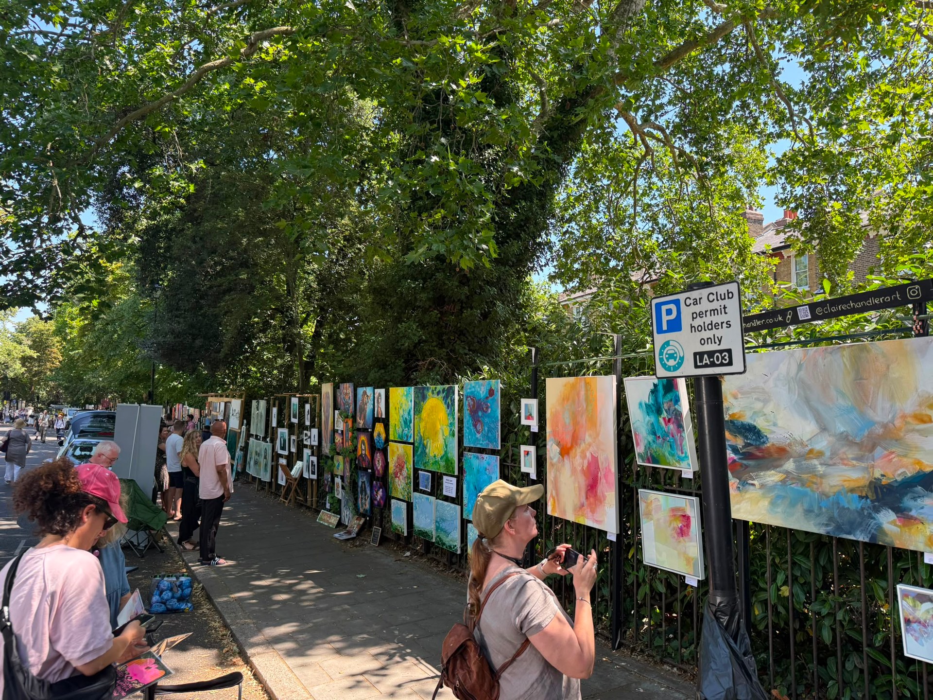 A row of colourful paintings and prints displayed outdoors at Brixton Urban Art Fair